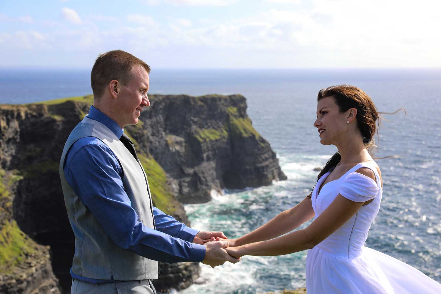 Holding hands during their wedding ceremony at The Cliffs of Moher