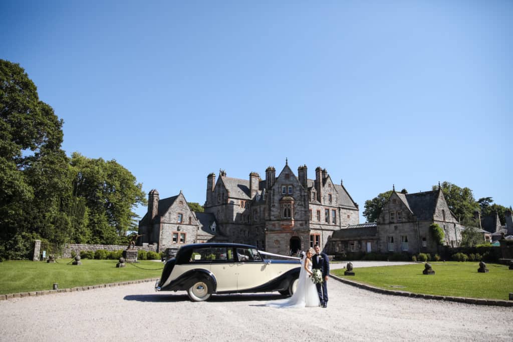 Couple pose with their car on their wedding day at Castle Leslie