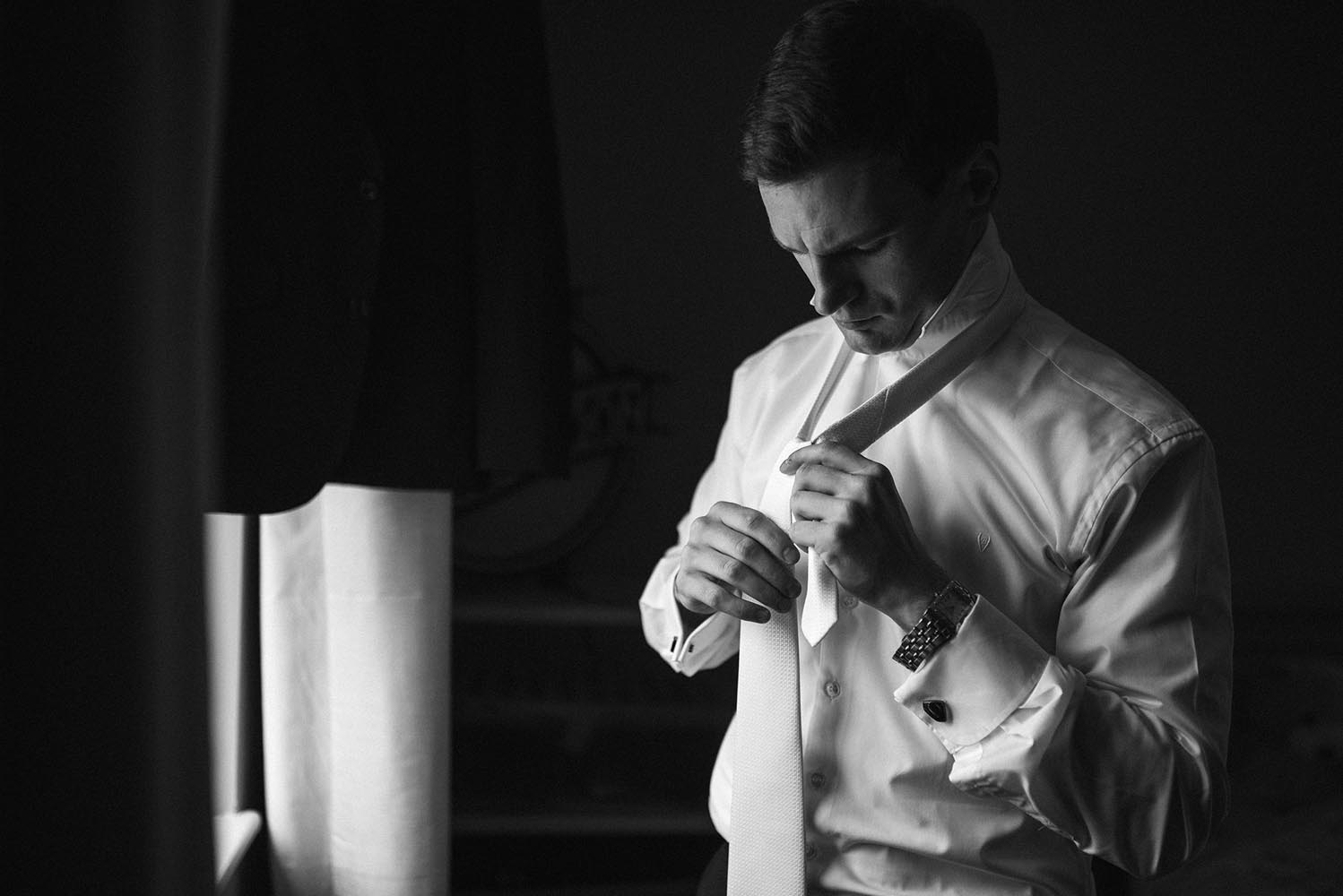 Groom tying his tie the morning of his wedding