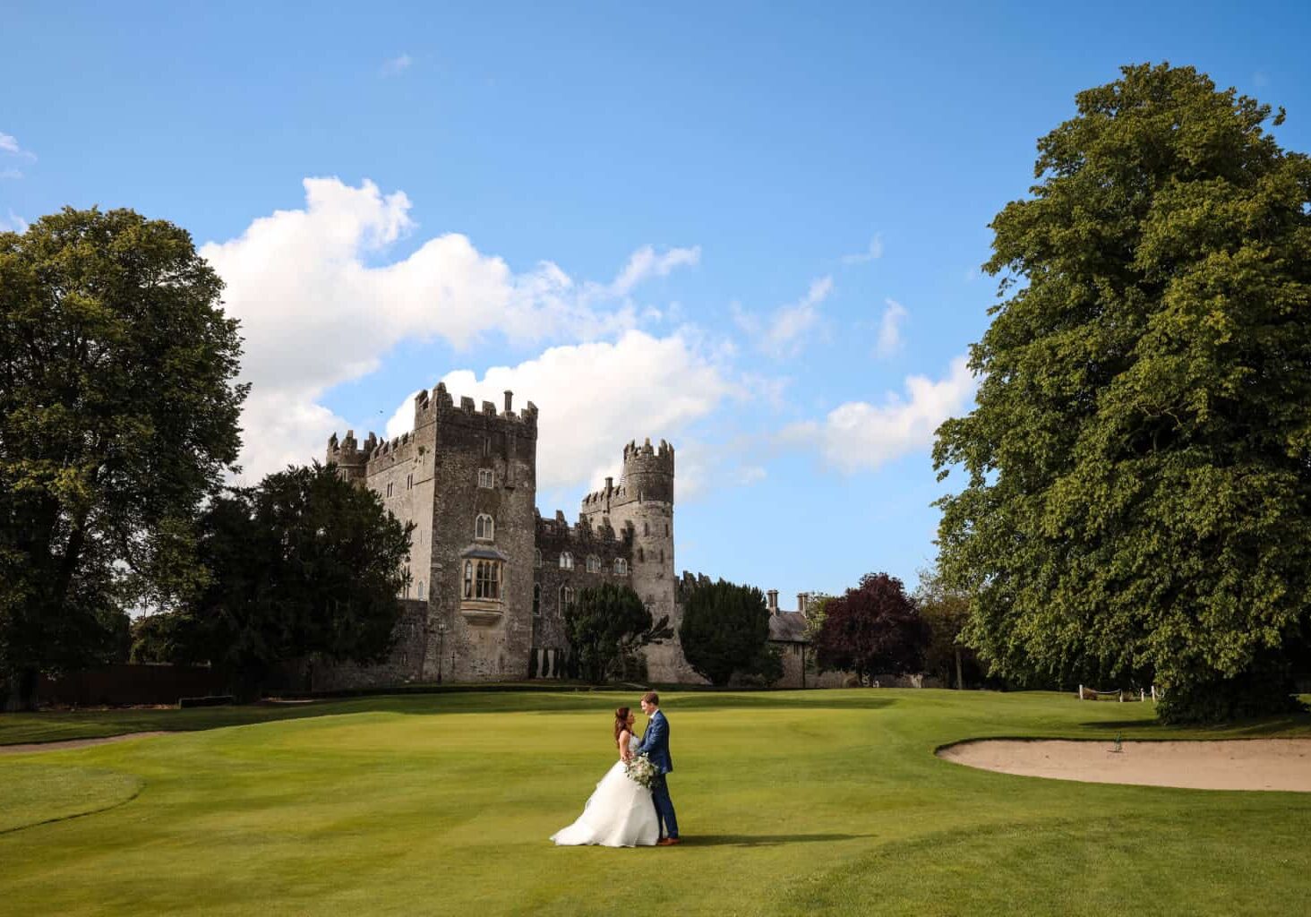 Bride and Groom embrace on the lawn in front of Kilkea Castle